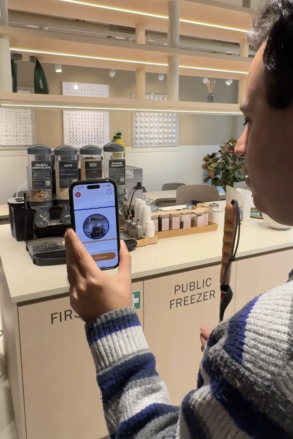 Someone at a café counter pointing a phone at a row of cereal dispensers and a coffee machine, Ally holding the photo it just took.