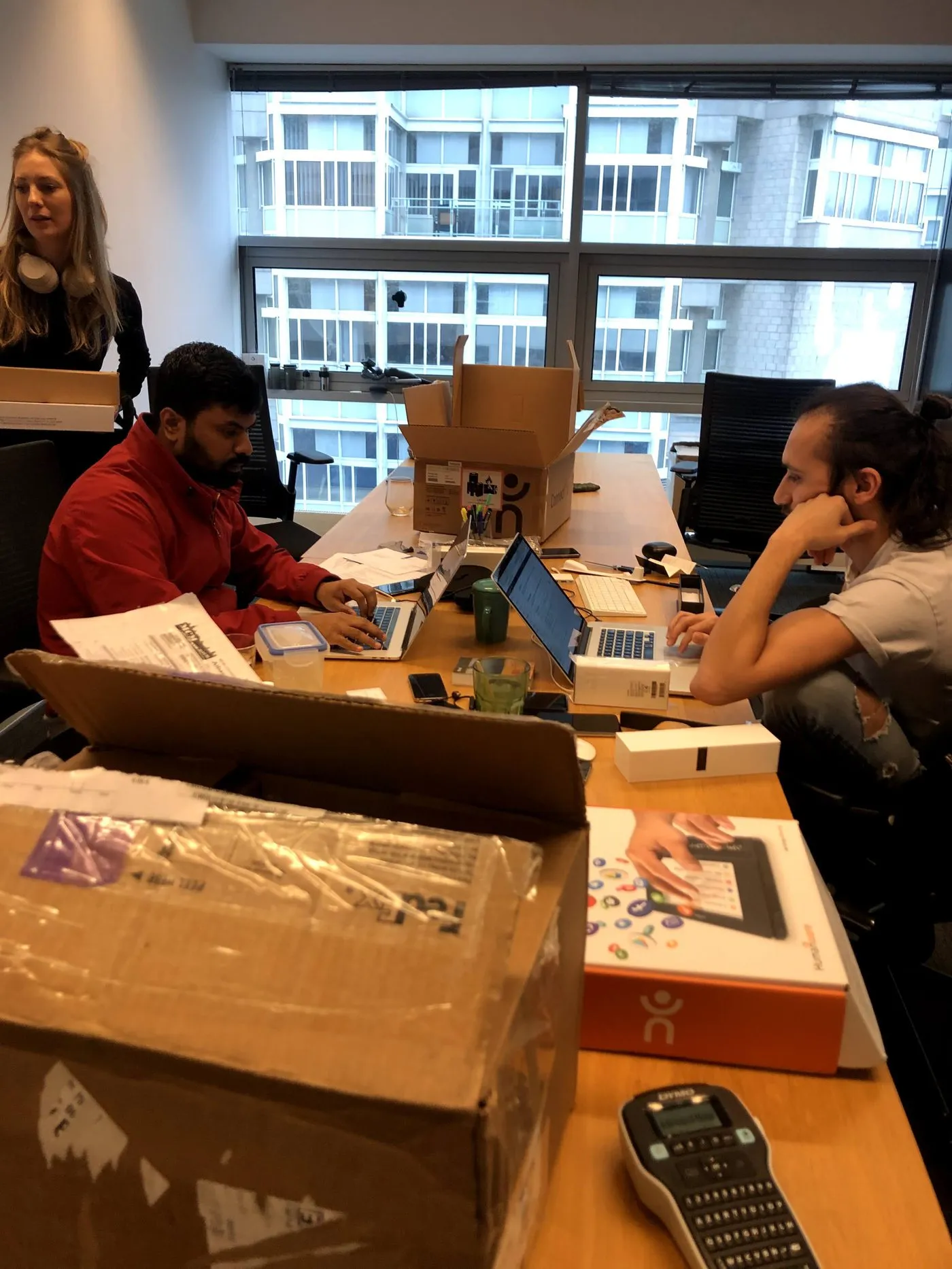 Our studio mid-build: the team around a table buried in cardboard boxes, packaging, laptops and a label printer, assembling and shipping the first units ourselves.