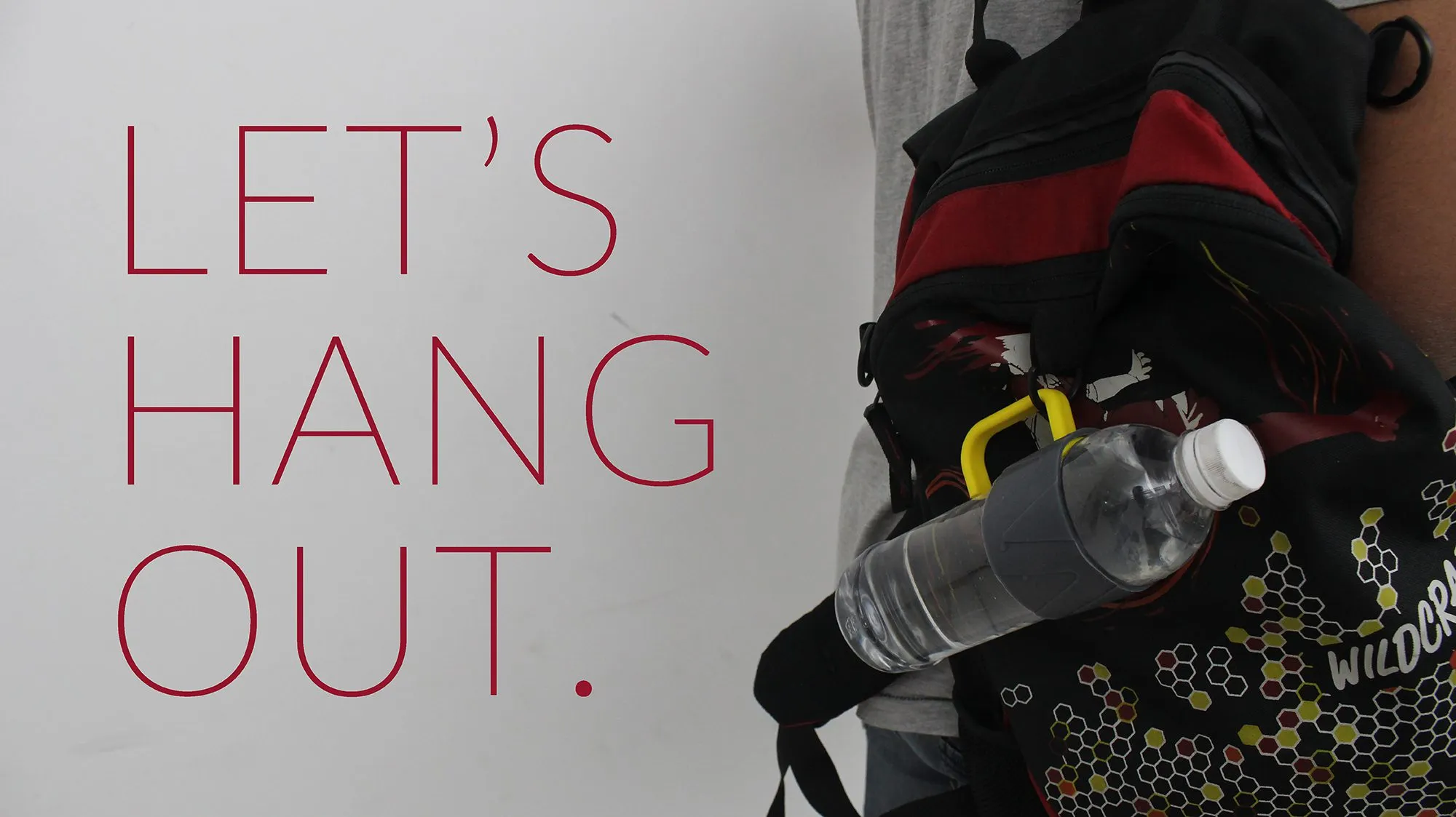 A water bottle hanging from a backpack strap by its yellow Jarry handle, with the words Let’s hang out