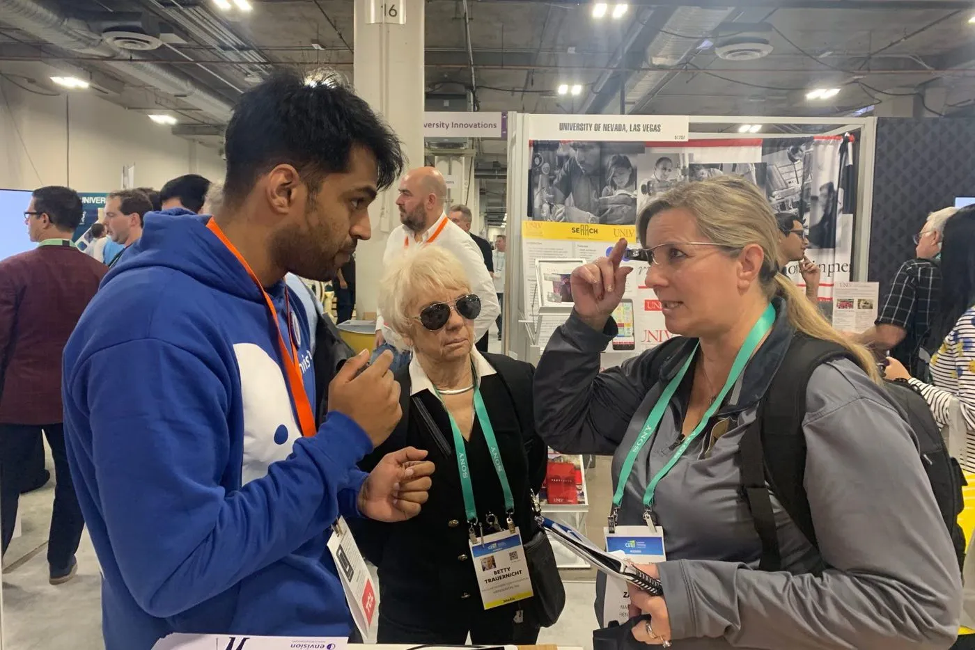 Me at our CES stand, mid-explanation, while a visitor tries a pair on and reaches up to feel the temple.