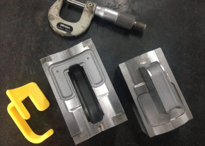The two halves of the aluminium injection mould for the handle, a micrometer beside them and a freshly moulded yellow handle still on its runner