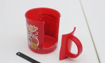 The red cup with its handle cut away, next to a steel ruler
