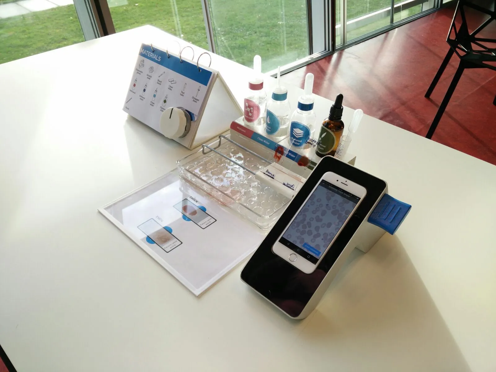 The kit as it was handed over: reagents, staining tray, slide guide, materials flip book, and the device mid scan.