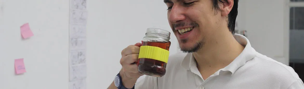 A colleague smiling mid-sip from the jar prototype at his desk, index cards pinned to the wall behind him