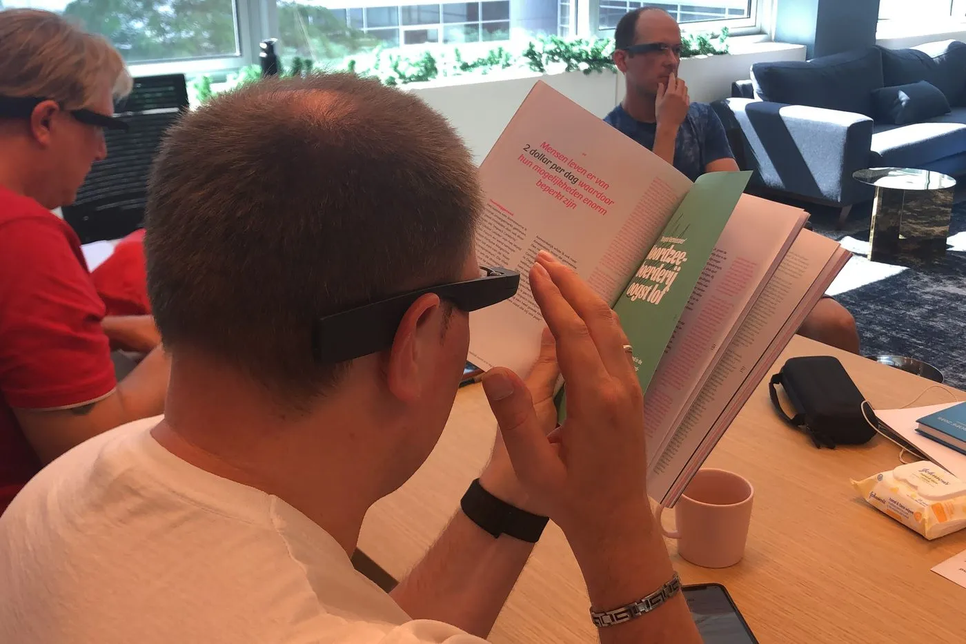 A user testing session in our office: three people wearing the glasses, one holding an open magazine up in front of him while it is read out to him.