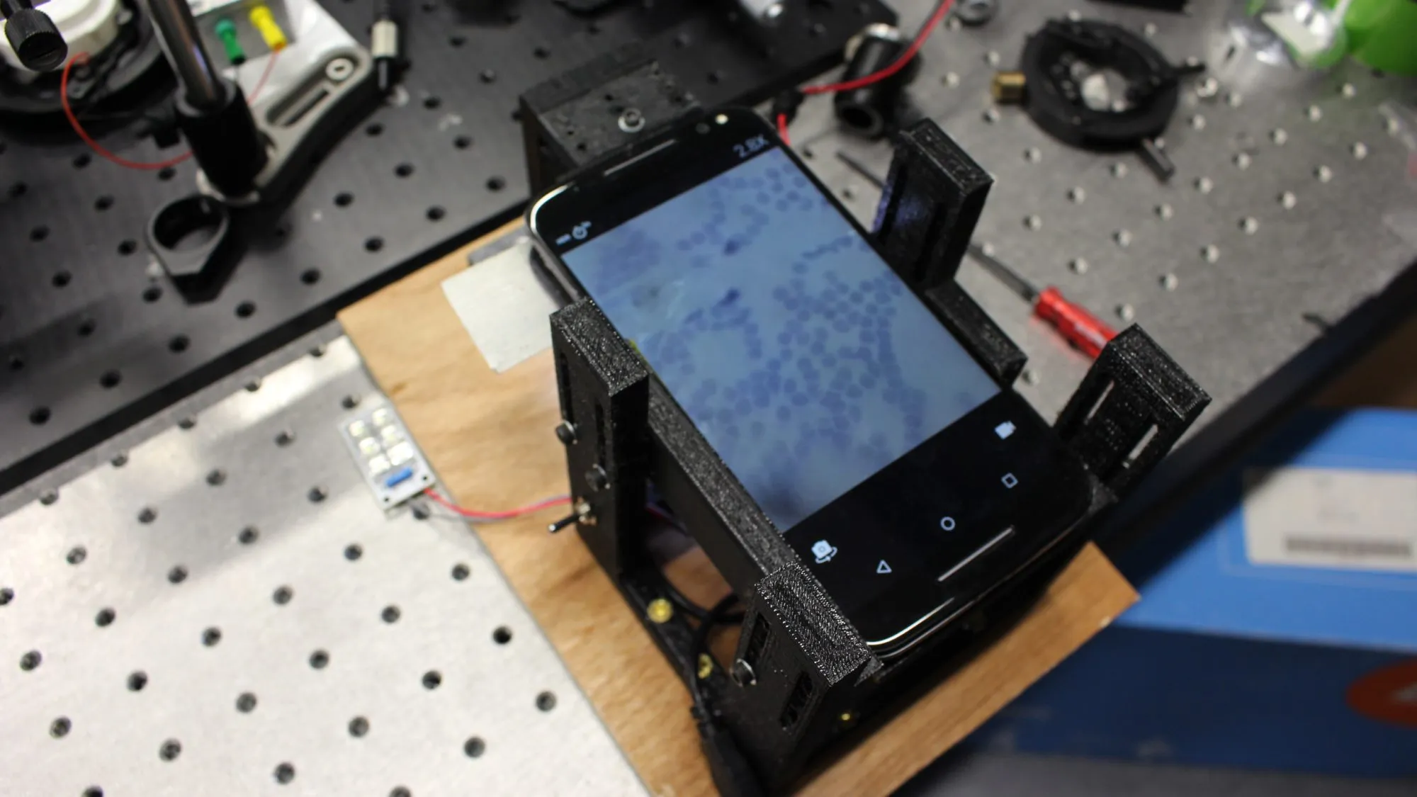 The working prototype: 3D printed frame, LED array, phone on top, stained cells on the screen.