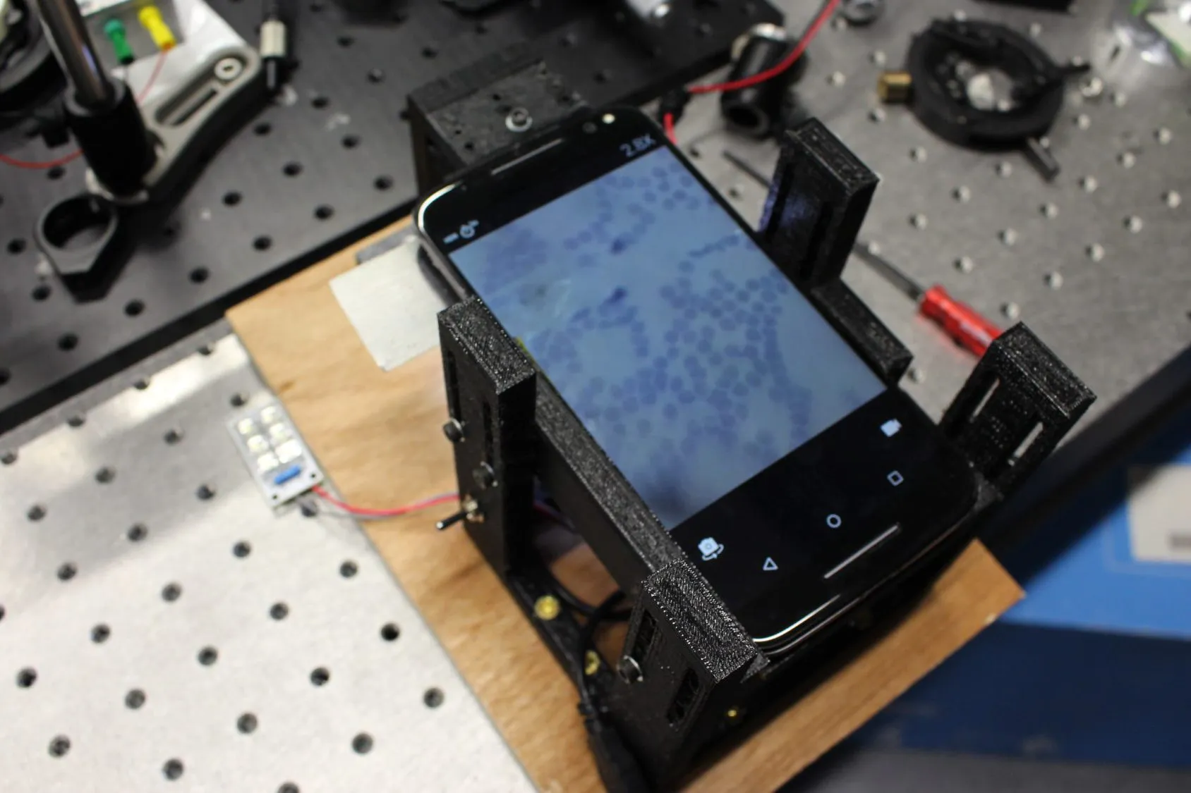 The working prototype: 3D printed frame, LED array, phone on top, stained cells on the screen.